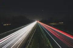An open highway at night, light trails running to a glow on the horizon