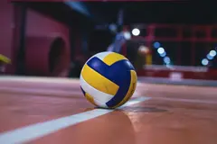 A volleyball on an indoor court under arena lights